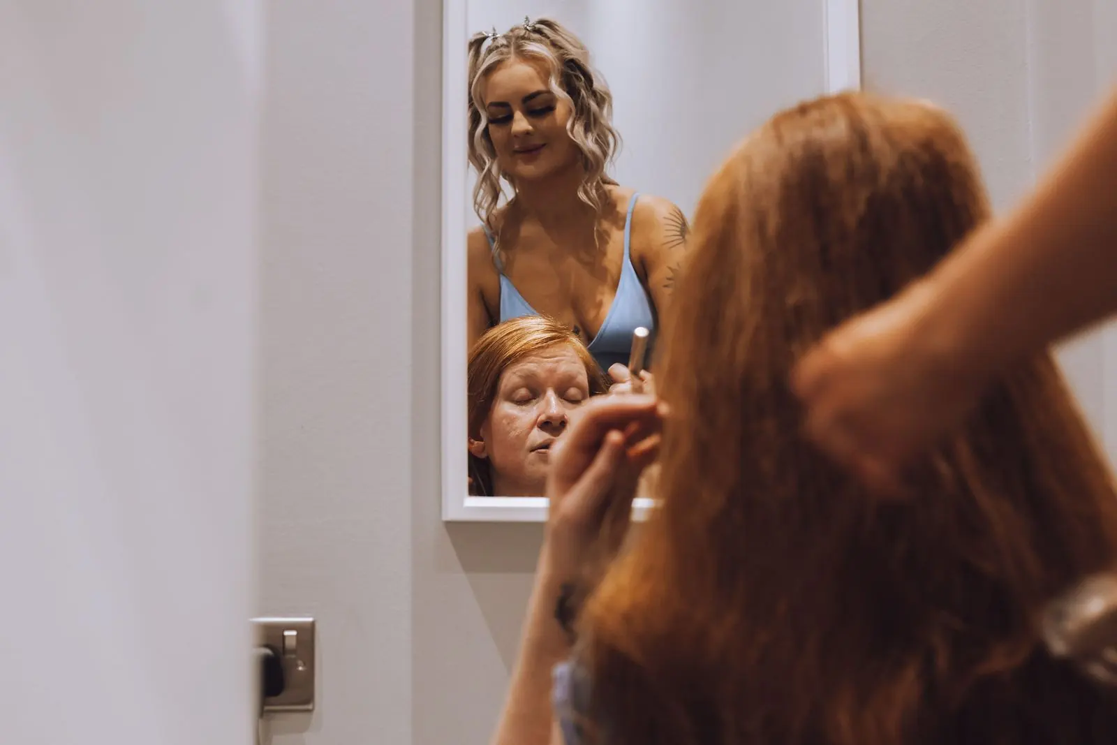 Bride having her hair styled, with bridesmaids reflected in the mirror