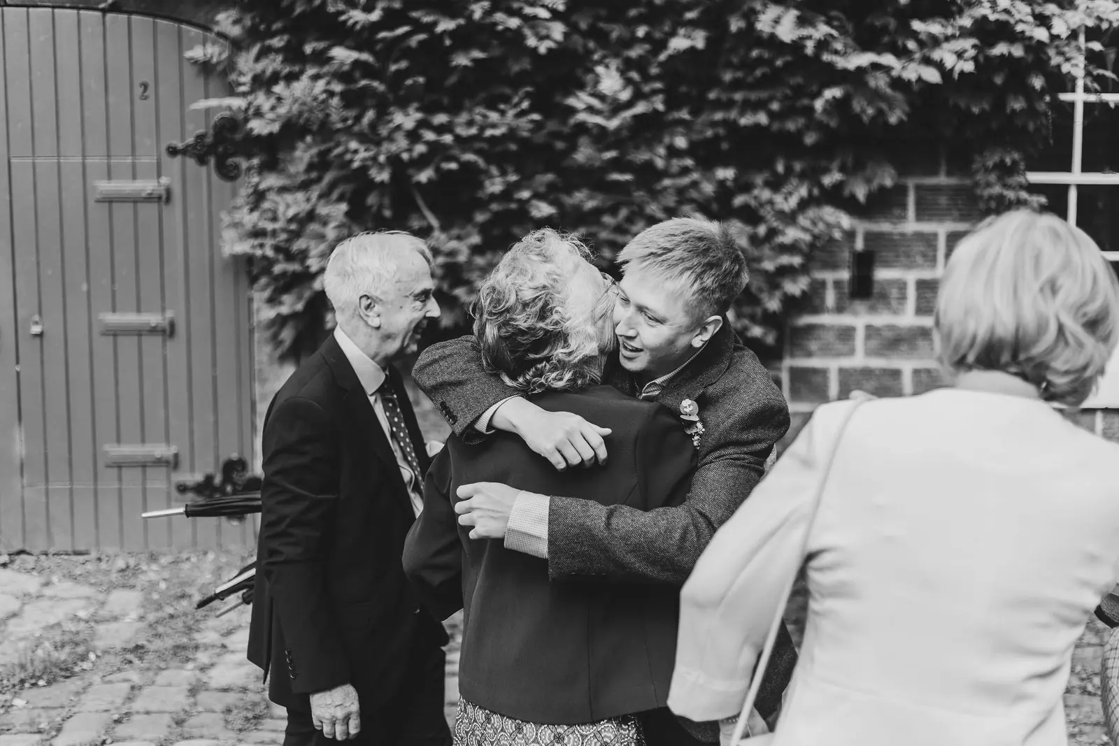 Family hugging outside before the ceremony, in black and white